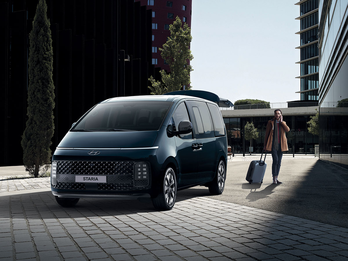 Un homme avec une valise marchant à côté du Hyundai Staria